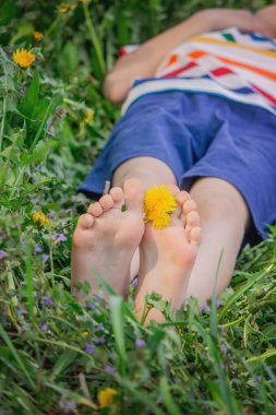 Yalınayak, yeşil çimenlerin üzerinde sarı karahindiba çiçekleri olan bir çocuğun resmini çek. Yaz mevsimi
