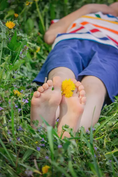 Yalınayak, yeşil çimenlerin üzerinde sarı karahindiba çiçekleri olan bir çocuğun resmini çek. Yaz mevsimi