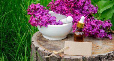 Ahşap bir kütükte leylak yağı. Kokulu yağ ve leylak çiçekli bir şişe..