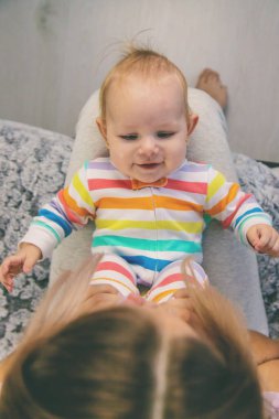 Anne kucağında küçük bir kız tutuyor, bacaklarıyla oynuyor ve ona masaj yapıyor. Bebeğim..