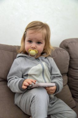 Kanepede oturan küçük kız telefonunu kullanıyor..