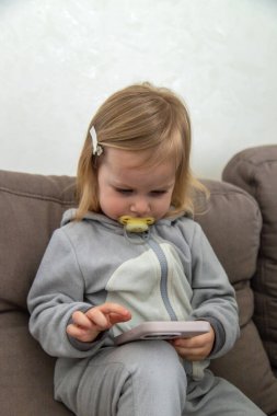 Kanepede oturan küçük kız telefonunu kullanıyor..