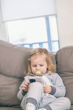 Kanepede oturan küçük kız telefonunu kullanıyor..