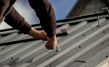 Bir adam çatıya güneş paneli monte ediyor. Seçici odak.