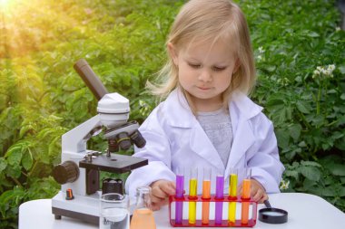 Küçük bir kız deney tüpleri, reaktörler ve mikroskop kullanarak deneyler yapıyor.