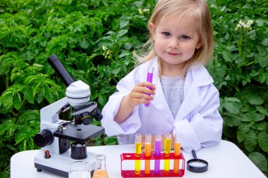 Küçük bir kız deney tüpleri, reaktörler ve mikroskop kullanarak deneyler yapıyor.