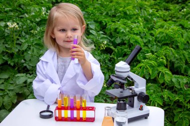 Küçük bir kız deney tüpleri, reaktörler ve mikroskop kullanarak deneyler yapıyor.