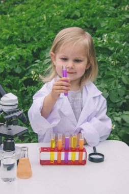 Küçük bir kız deney tüpleri, reaktörler ve mikroskop kullanarak deneyler yapıyor.