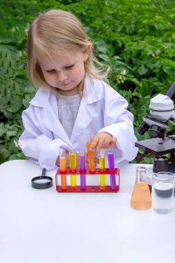 Küçük bir kız deney tüpleri, reaktörler ve mikroskop kullanarak deneyler yapıyor.