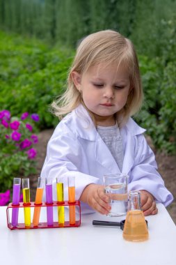 Küçük bir kız deney tüpleri, reaktörler ve mikroskop kullanarak deneyler yapıyor.