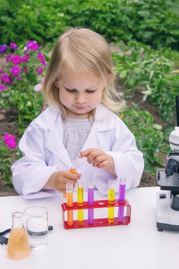 Küçük bir kız deney tüpleri, reaktörler ve mikroskop kullanarak deneyler yapıyor.