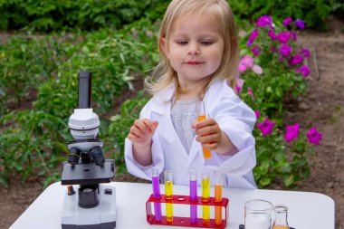Küçük bir kız deney tüpleri, reaktörler ve mikroskop kullanarak deneyler yapıyor.