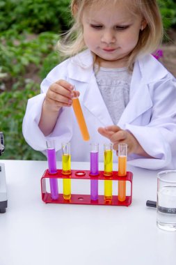 Küçük bir kız deney tüpleri, reaktörler ve mikroskop kullanarak deneyler yapıyor.
