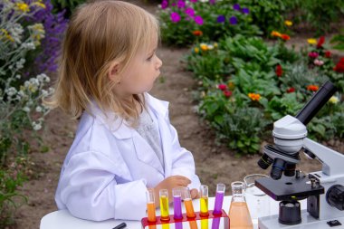 Küçük bir kız deney tüpleri, reaktörler ve mikroskop kullanarak deneyler yapıyor.