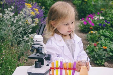 Küçük bir kız deney tüpleri, reaktörler ve mikroskop kullanarak deneyler yapıyor.