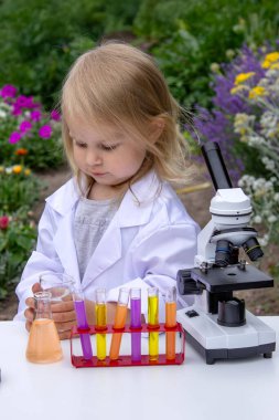 Küçük bir kız deney tüpleri, reaktörler ve mikroskop kullanarak deneyler yapıyor.