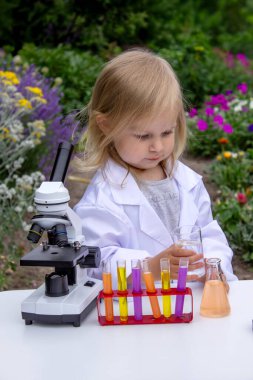 Küçük bir kız deney tüpleri, reaktörler ve mikroskop kullanarak deneyler yapıyor.