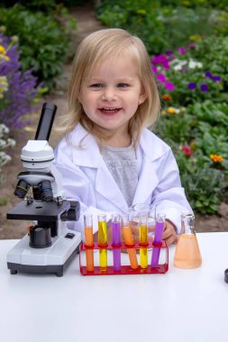 Küçük bir kız deney tüpleri, reaktörler ve mikroskop kullanarak deneyler yapıyor.