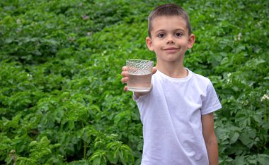 Çocuk bardaktan su içiyor doğanın arka planına karşı..