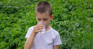 Çocuk bardaktan su içiyor doğanın arka planına karşı..