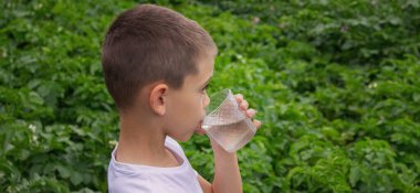 Çocuk bardaktan su içiyor doğanın arka planına karşı..