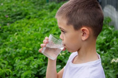 Çocuk bardaktan su içiyor doğanın arka planına karşı..