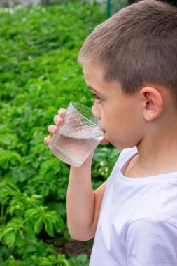 Çocuk bardaktan su içiyor doğanın arka planına karşı..