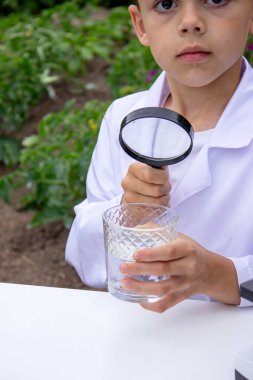 Bir çocuk suyu büyüteçle inceler..