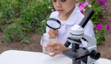 Bir çocuk suyu büyüteçle inceler..