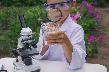 Bir çocuk suyu büyüteçle inceler..