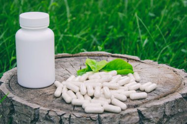 Kapsüllerde bitkisel ilaçlar, ağaç gövdesinde bitki yaprakları.