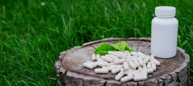 Kapsüllerde bitkisel ilaçlar, ağaç gövdesinde bitki yaprakları.