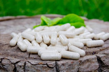 Kapsüllerde bitkisel ilaçlar, ağaç gövdesinde bitki yaprakları.