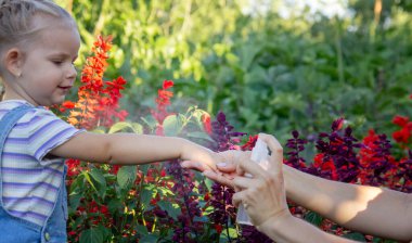 Bir anne çocuğuna sivrisinek kovucu sıkar.