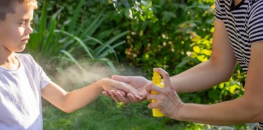 Anne, yaz bahçesinde çocuklara sivrisinek kovucu sıkar..