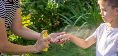 Anne, yaz bahçesinde çocuklara sivrisinek kovucu sıkar..