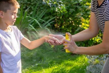 Anne, yaz bahçesinde çocuklara sivrisinek kovucu sıkar..