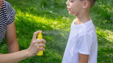 Anne, yaz bahçesinde çocuklara sivrisinek kovucu sıkar..