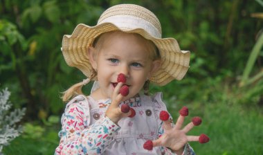 Bahçede ahududu yiyen küçük bir kız. Parmaklarında ahududu var.