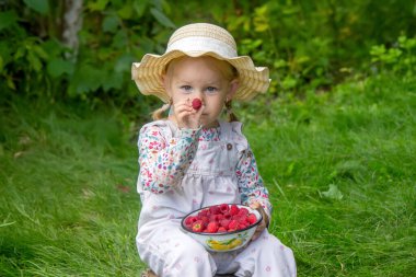Bahçede ahududu yiyen küçük bir kız. Parmaklarında ahududu var.
