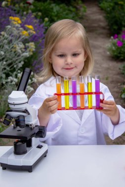 Küçük bir kız deney tüpleri, reaktörler ve mikroskop kullanarak deneyler yapıyor.