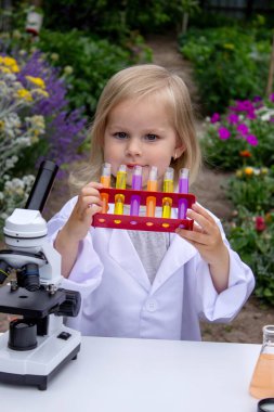 Küçük bir kız deney tüpleri, reaktörler ve mikroskop kullanarak deneyler yapıyor.