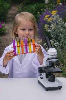 Küçük bir kız deney tüpleri, reaktörler ve mikroskop kullanarak deneyler yapıyor.
