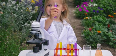 Küçük bir kız deney tüpleri, reaktörler ve mikroskop kullanarak deneyler yapıyor.