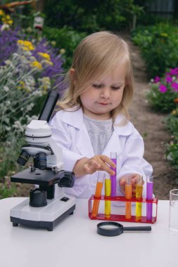 Küçük bir kız deney tüpleri, reaktörler ve mikroskop kullanarak deneyler yapıyor.