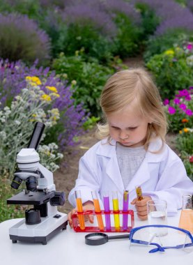 Küçük bir kız deney tüpleri, reaktörler ve mikroskop kullanarak deneyler yapıyor.