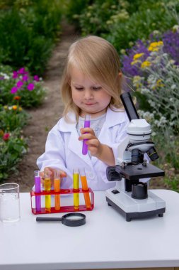 Küçük bir kız deney tüpleri, reaktörler ve mikroskop kullanarak deneyler yapıyor.