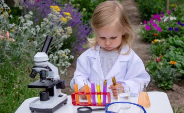 Küçük bir kız deney tüpleri, reaktörler ve mikroskop kullanarak deneyler yapıyor.