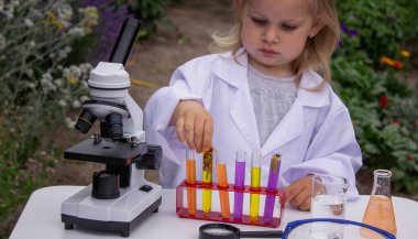 Küçük bir kız deney tüpleri, reaktörler ve mikroskop kullanarak deneyler yapıyor.