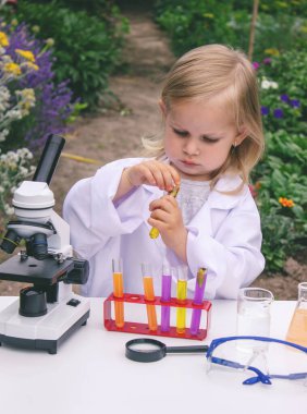 Küçük bir kız deney tüpleri, reaktörler ve mikroskop kullanarak deneyler yapıyor.
